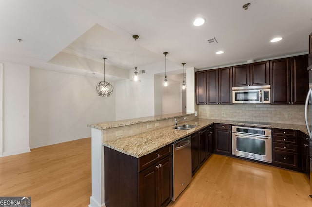 kitchen featuring sink, appliances with stainless steel finishes, hanging light fixtures, light stone counters, and kitchen peninsula