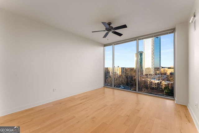 empty room with ceiling fan, a wall of windows, and light hardwood / wood-style floors