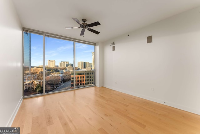 spare room with hardwood / wood-style flooring, ceiling fan, and a wall of windows