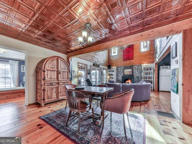 dining area with a stone fireplace, light hardwood / wood-style flooring, and a notable chandelier