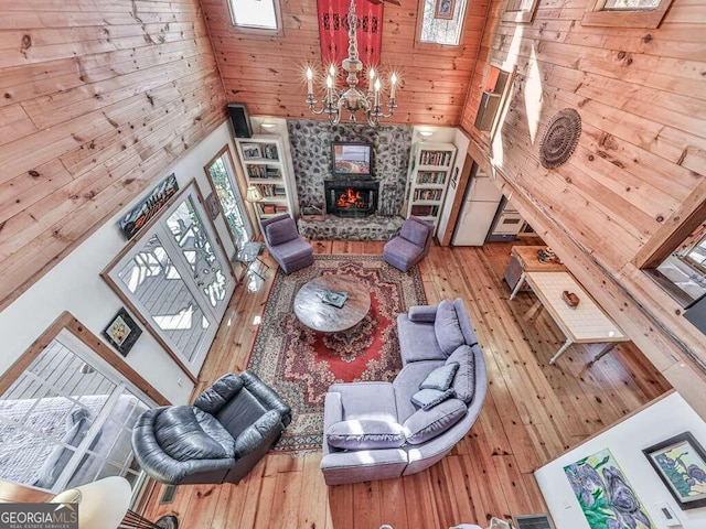 living room with wood walls, a wood stove, high vaulted ceiling, light wood-type flooring, and a notable chandelier