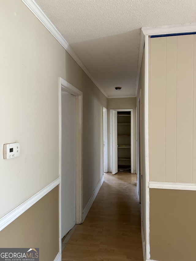 corridor with a textured ceiling, light wood-style flooring, baseboards, and ornamental molding