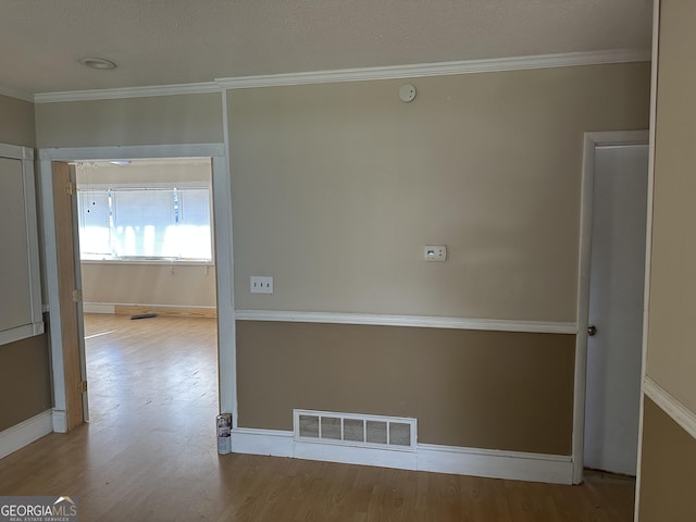 empty room featuring baseboards, visible vents, wood finished floors, and ornamental molding