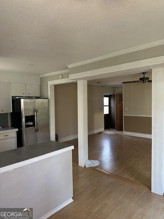 kitchen with crown molding, stainless steel refrigerator with ice dispenser, a textured ceiling, wood finished floors, and baseboards