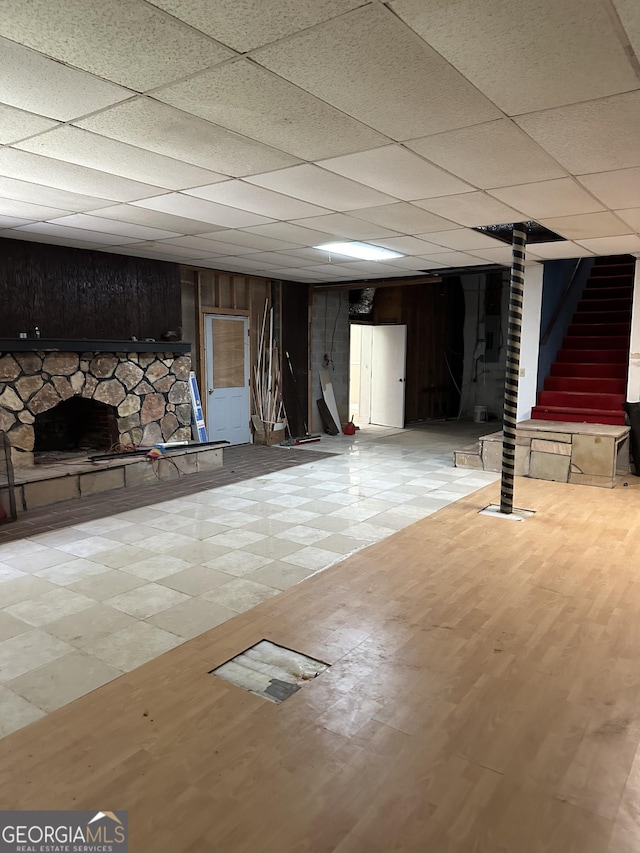 finished basement with stairway, a drop ceiling, and wood finished floors