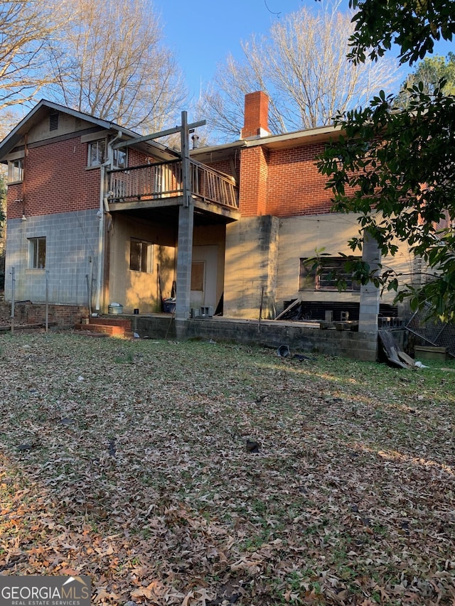 back of house with brick siding, a chimney, and a deck