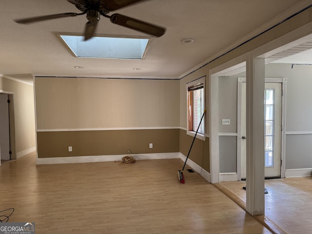 spare room featuring crown molding, baseboards, light wood-style flooring, a skylight, and a ceiling fan