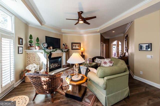 living room featuring a tray ceiling, ceiling fan, dark wood-type flooring, and ornamental molding