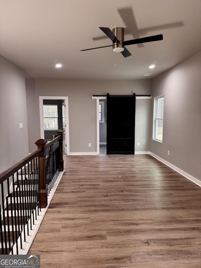 unfurnished living room featuring hardwood / wood-style flooring, ceiling fan, a barn door, and a healthy amount of sunlight