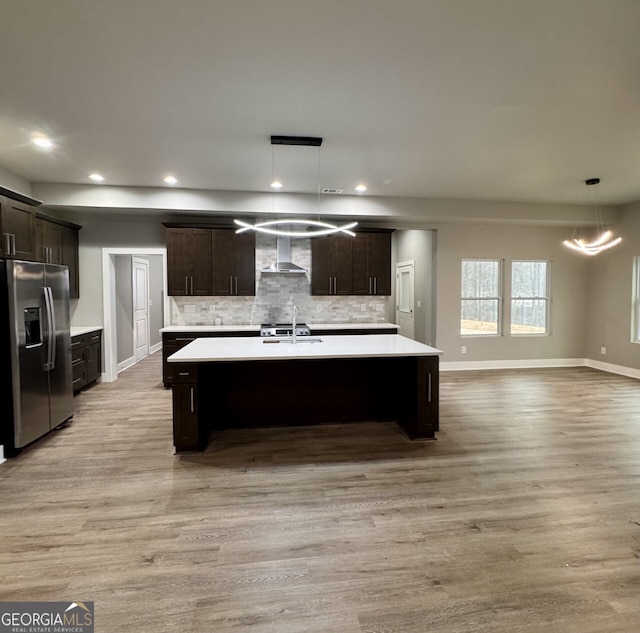 kitchen with hanging light fixtures, sink, stainless steel fridge, and wall chimney exhaust hood