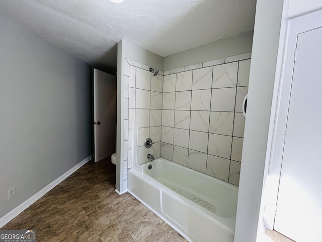 bathroom with toilet, a textured ceiling, and tiled shower / bath