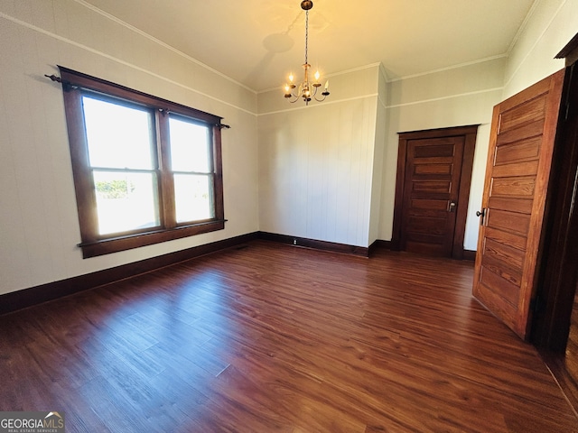 spare room featuring crown molding, dark wood-type flooring, and a notable chandelier