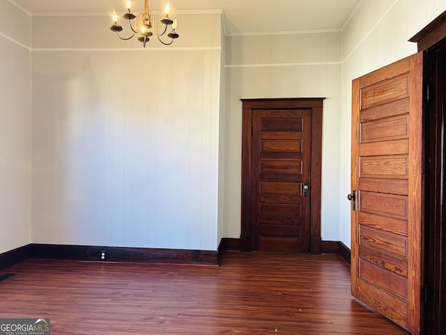 empty room with a chandelier, dark wood-type flooring, wood walls, and ornamental molding