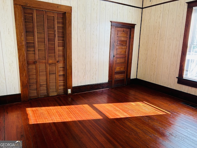 unfurnished bedroom with wood walls, dark wood-type flooring, and a closet