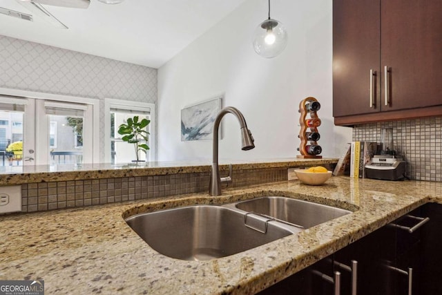 kitchen featuring a sink, hanging light fixtures, decorative backsplash, and light stone countertops