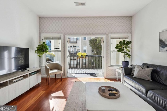 living area featuring an accent wall, visible vents, and wallpapered walls