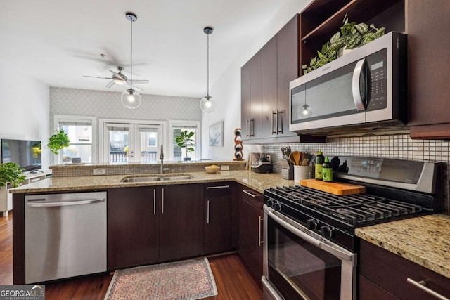 kitchen with light stone counters, decorative light fixtures, stainless steel appliances, a sink, and a peninsula