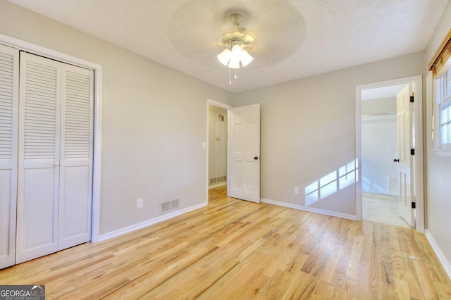 unfurnished bedroom featuring a textured ceiling, a closet, light hardwood / wood-style floors, and ceiling fan