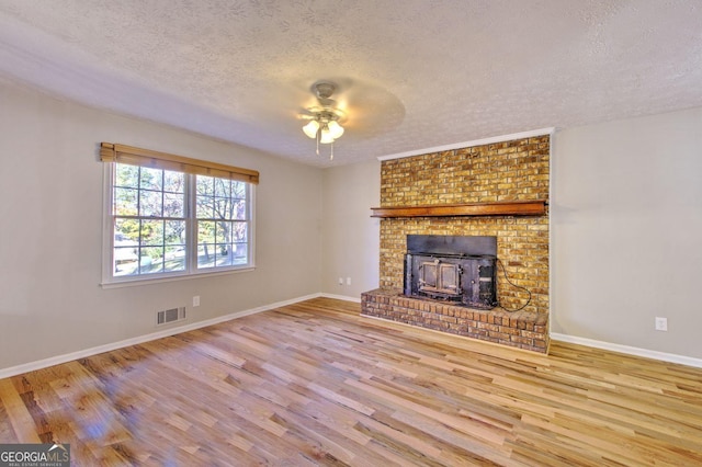 unfurnished living room featuring ceiling fan, light hardwood / wood-style floors, a wood stove, and a textured ceiling