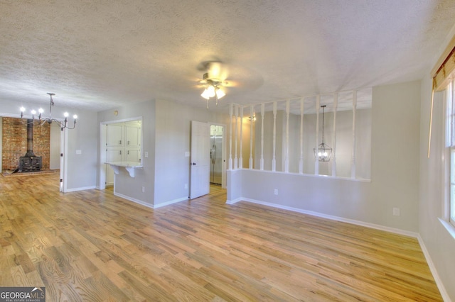 interior space with a wood stove, light hardwood / wood-style flooring, plenty of natural light, a textured ceiling, and ceiling fan with notable chandelier