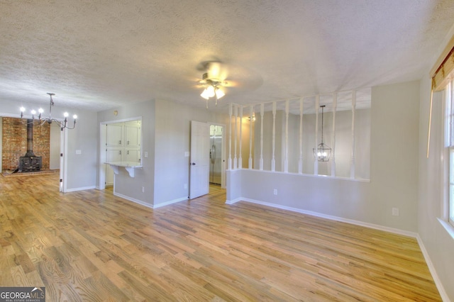 1304 Vine St NE, Gainesville, GA 30501 - unfurnished living room featuring a wood stove, light wood finished floors, a textured ceiling, a chandelier, and a ceiling fan
