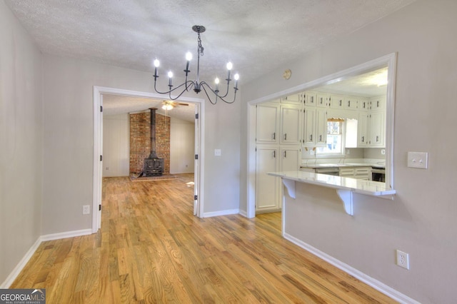 kitchen featuring a wood stove, a kitchen breakfast bar, a textured ceiling, light hardwood / wood-style floors, and white cabinetry