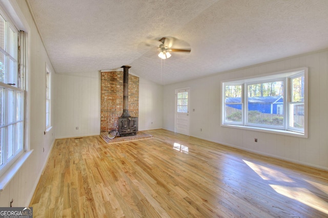 unfurnished living room with a textured ceiling, vaulted ceiling, ceiling fan, light hardwood / wood-style floors, and a wood stove