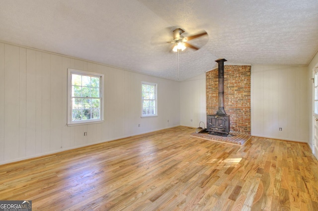 unfurnished living room with a textured ceiling, vaulted ceiling, light hardwood / wood-style floors, and a wood stove