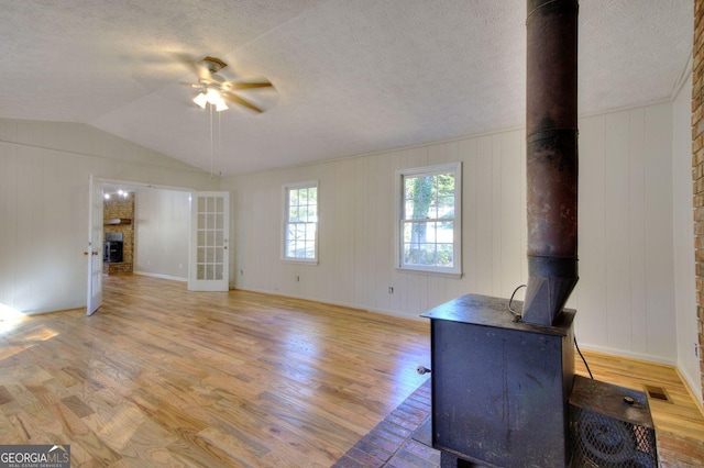 unfurnished living room featuring light wood-type flooring, a wood stove, and ceiling fan