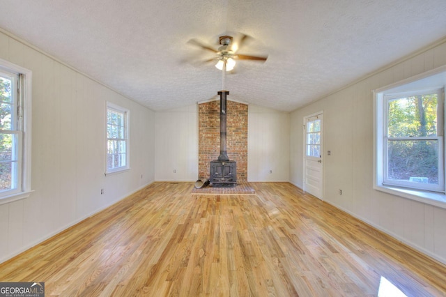 unfurnished living room with a wood stove, a textured ceiling, light hardwood / wood-style floors, and vaulted ceiling