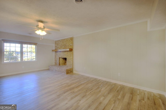 unfurnished living room featuring light wood-type flooring, a brick fireplace, ornamental molding, a textured ceiling, and ceiling fan