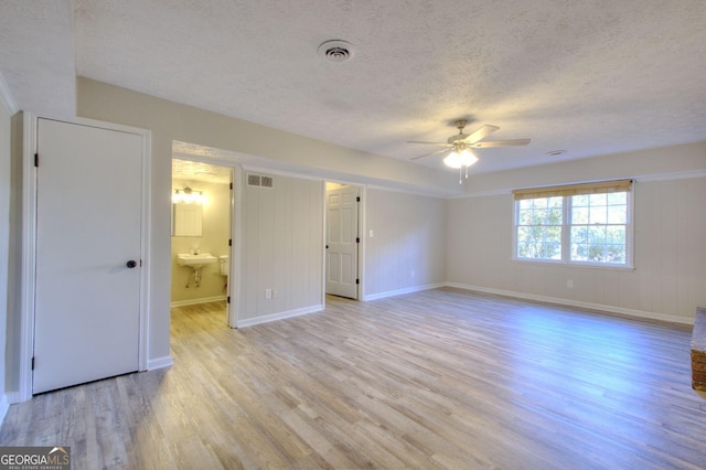 unfurnished bedroom featuring ceiling fan, sink, light hardwood / wood-style flooring, ensuite bathroom, and a textured ceiling