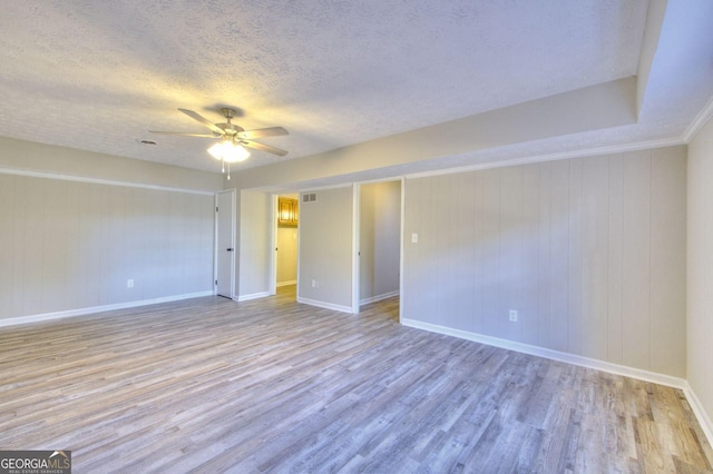 unfurnished room with ceiling fan, light hardwood / wood-style flooring, a textured ceiling, and wooden walls