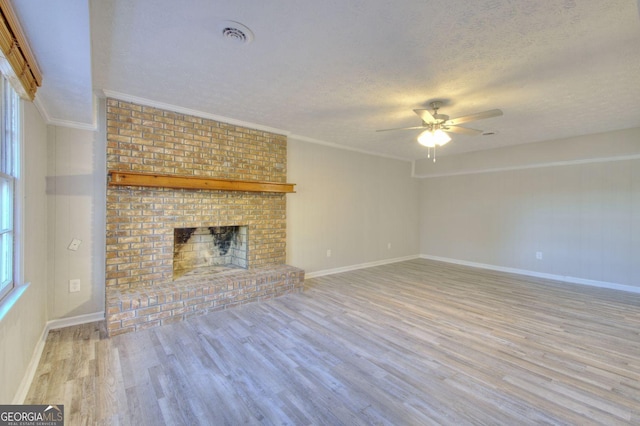 unfurnished living room featuring ceiling fan, a brick fireplace, light hardwood / wood-style flooring, a textured ceiling, and ornamental molding