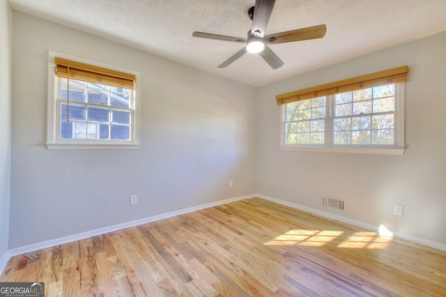 empty room featuring ceiling fan, a healthy amount of sunlight, light wood-type flooring, and a textured ceiling