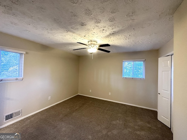 unfurnished room featuring ceiling fan, dark carpet, and a textured ceiling