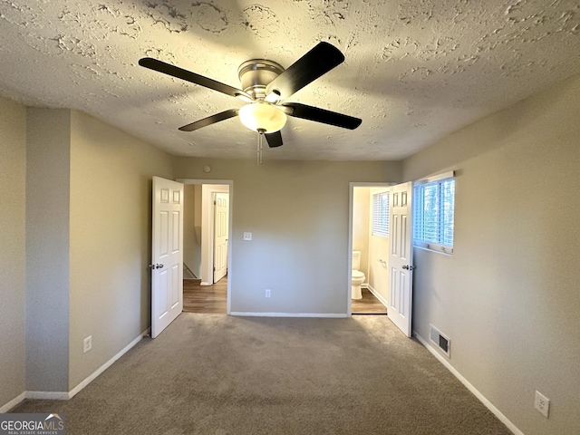 unfurnished bedroom with ceiling fan, ensuite bathroom, dark carpet, and a textured ceiling