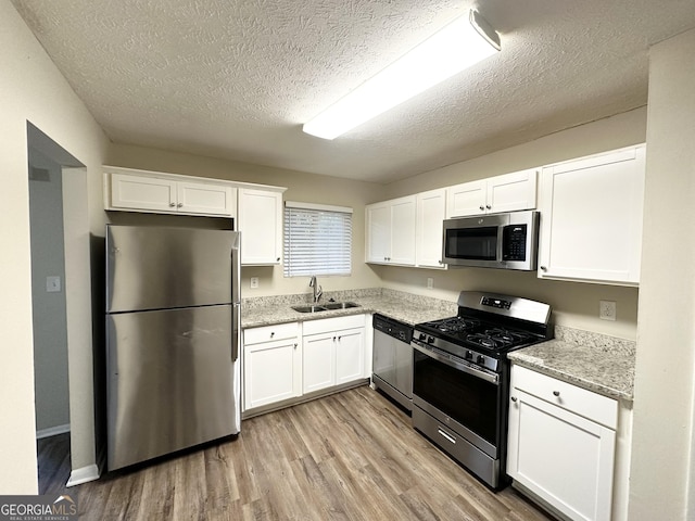 kitchen with light wood-type flooring, a textured ceiling, stainless steel appliances, sink, and white cabinets