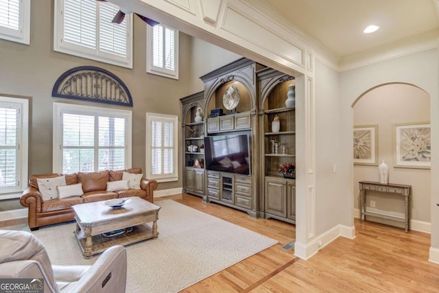 living room featuring a high ceiling, light wood-type flooring, and ornamental molding