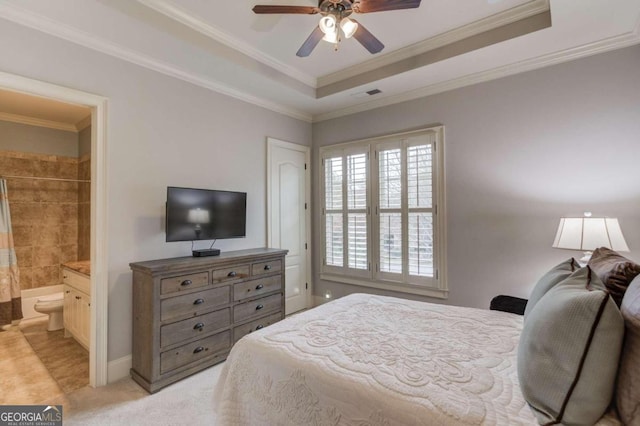 carpeted bedroom with ensuite bathroom, ceiling fan, ornamental molding, and a tray ceiling