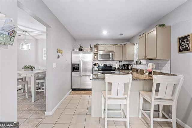 kitchen featuring sink, stainless steel appliances, kitchen peninsula, dark stone counters, and a breakfast bar