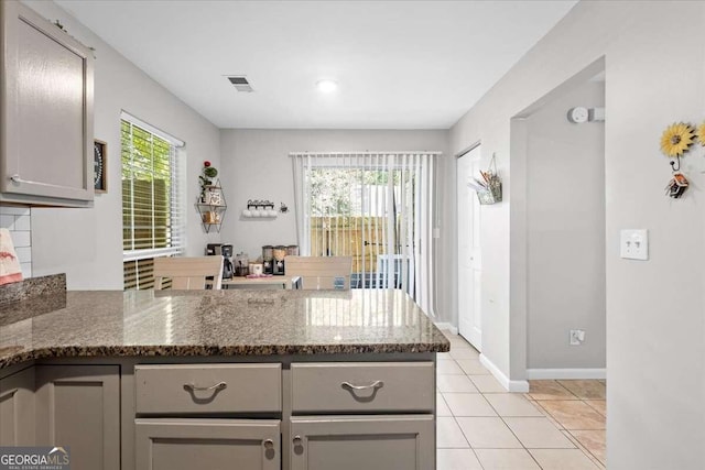 kitchen with kitchen peninsula, dark stone counters, gray cabinets, and a healthy amount of sunlight