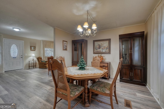 dining space featuring ornamental molding, a textured ceiling, light hardwood / wood-style floors, and a notable chandelier