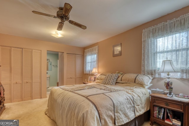 bedroom featuring carpet flooring, two closets, ensuite bath, and ceiling fan