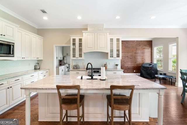 kitchen featuring a breakfast bar area, light stone countertops, an island with sink, and appliances with stainless steel finishes