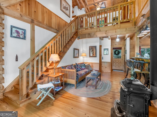 living room featuring light wood-type flooring, a wood stove, a high ceiling, and wooden walls