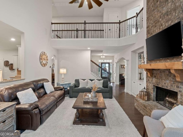 living room featuring ceiling fan, dark hardwood / wood-style flooring, a high ceiling, and a brick fireplace