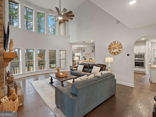 living room featuring a brick fireplace, high vaulted ceiling, ceiling fan, and dark wood-type flooring