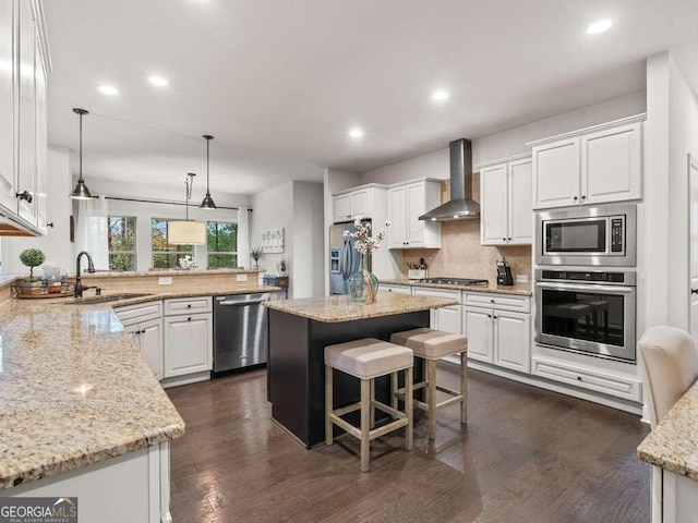 kitchen with white cabinets, appliances with stainless steel finishes, a kitchen island, and wall chimney exhaust hood