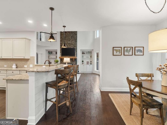 kitchen with pendant lighting, a breakfast bar, light stone counters, dark hardwood / wood-style flooring, and white cabinetry